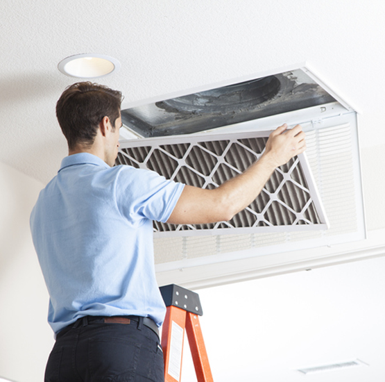 Technician replacing a ceiling return air filter in a home